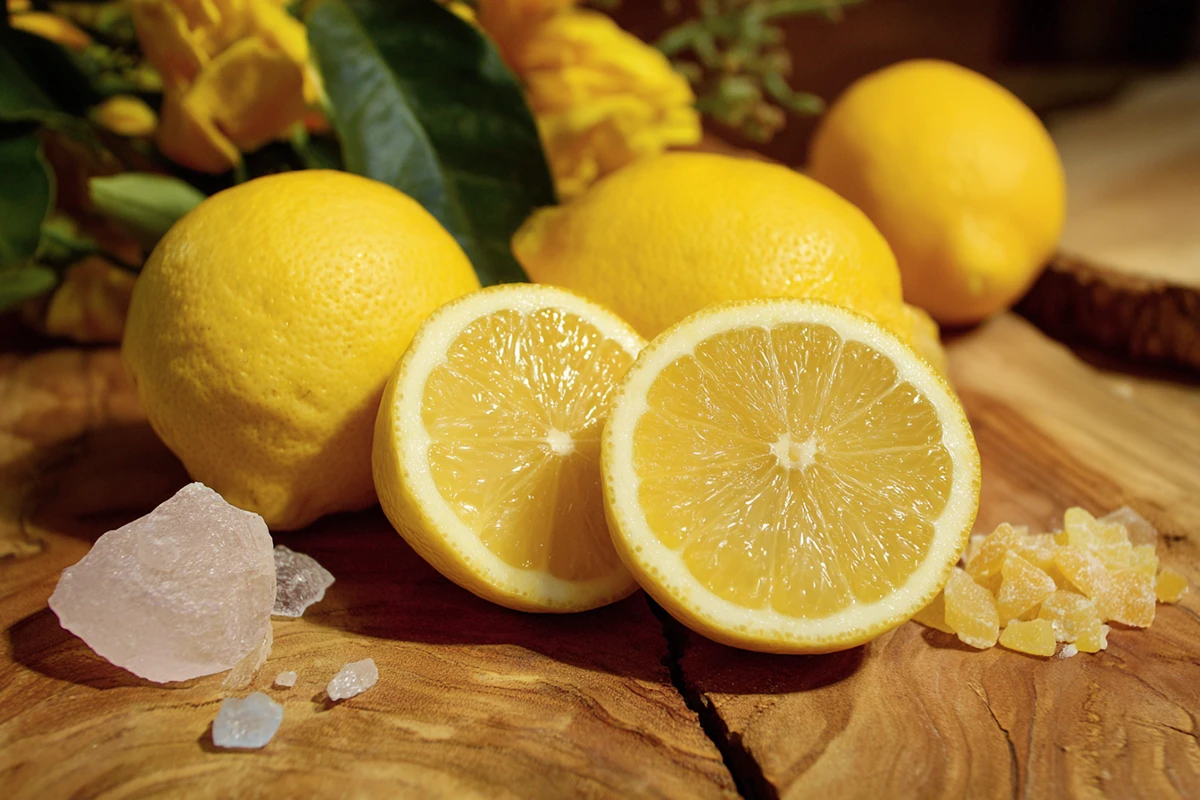 Whole and halved lemons displayed with crystals and candied lemon peel on a wooden surface